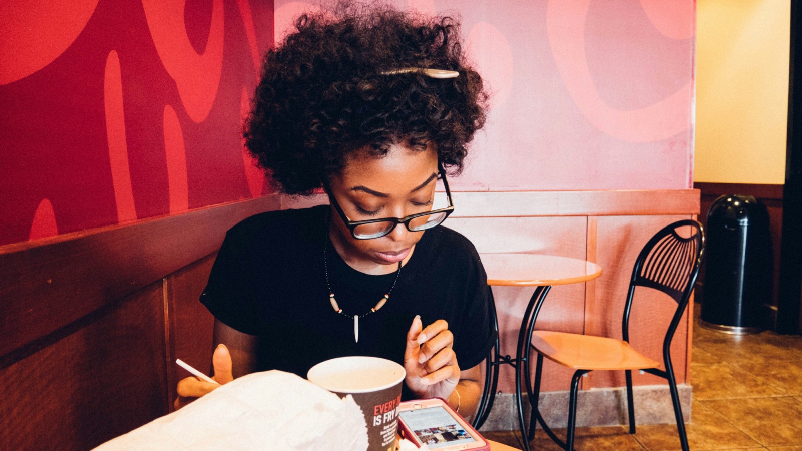Someone in glasses checks their phone at a café table, a coffee cup in front of them