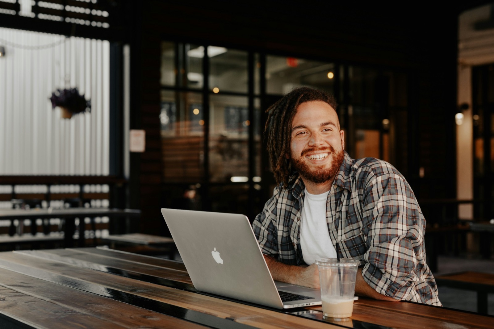 Someone smiling at an outdoor table with a laptop and an iced coffee